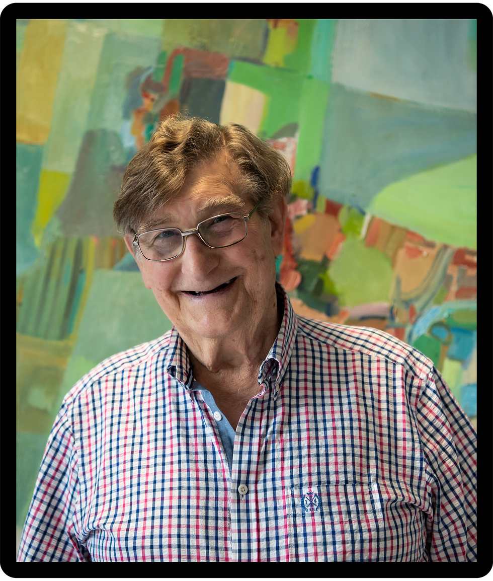 Smiling elderly man in glasses and a red-blue checkered shirt stands before a colorful abstract painting backdrop.