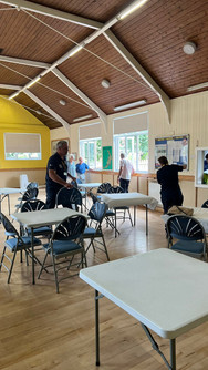 Indoor hall with two man setting up tables and chairs.