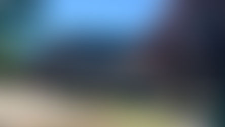 Brick building with gabled entrance, surrounded by greenery under blue sky. Signposts point to various locations. Calm, sunny day.