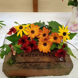 Yellow, orange and dark red flowers displayed on an old brick made in Southwater.
