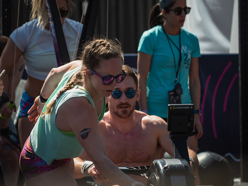 Coach Nicole leaning in to help adjust the damper setting on a concept 2 rower for her teammate at t