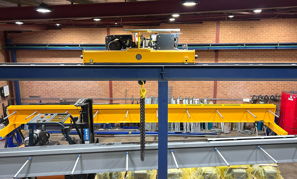 Large crane lifts object at industrial site with gantry structure, pipes, and safety barriers.