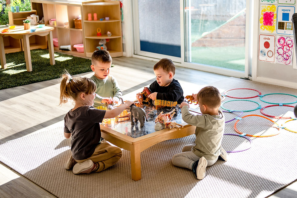 Four children playing with animal figurines together around a classroom table
