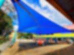 Large blue shade structure installation in progress or recently completed over a paved area beside a building.