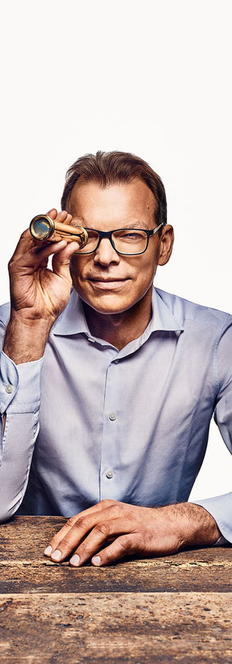 Elder man, sitting on a table, holding a caleidoscope in front of his eye