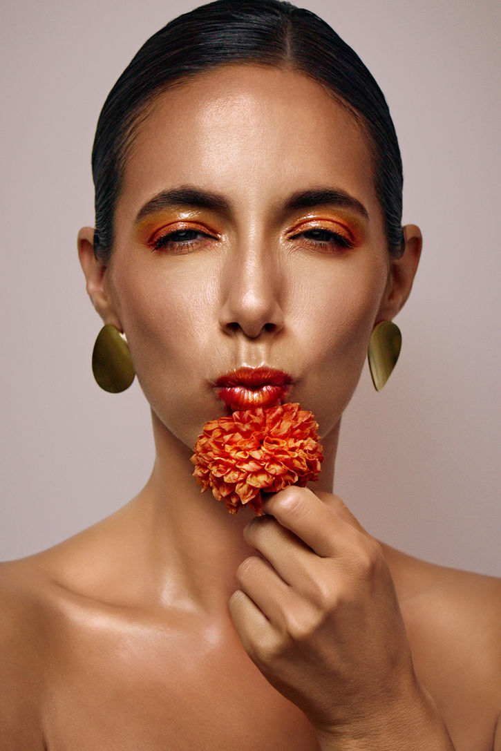 Close-up beauty portrait of a model with golden earrings and orange flower, bold makeup and glossy skin – shot by Erik Bont