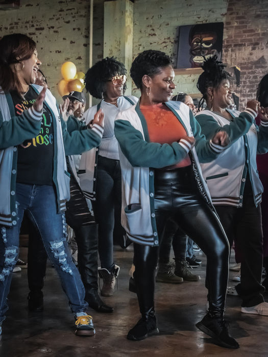 Group of women dancing with matching jackets indoors, smiling and posing.