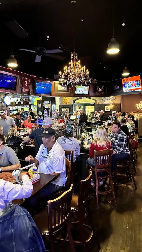 Customers sitting at tables and bar in a bustling, lively bar setting.
