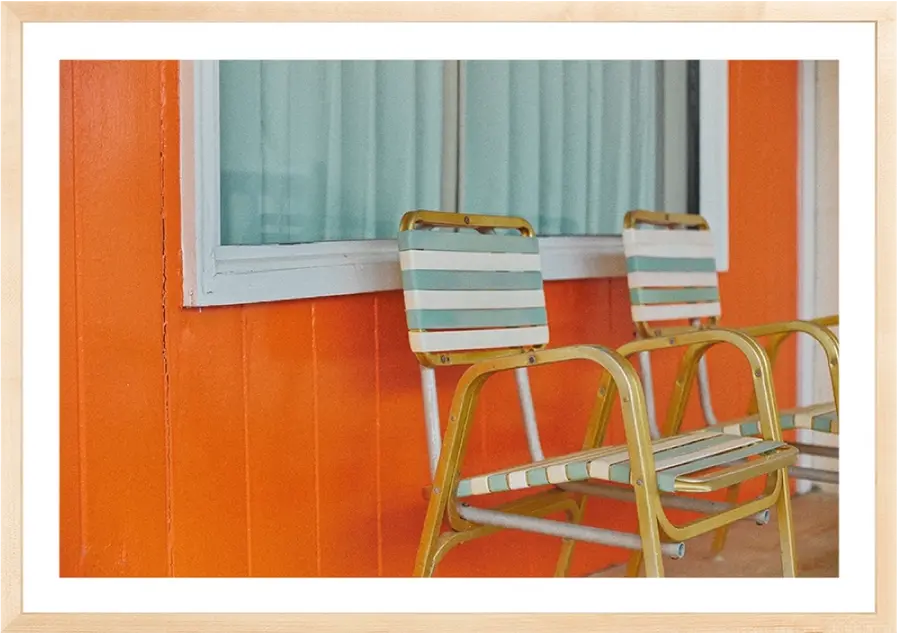 Two vintage chairs sit on a porch against an orange wall background.