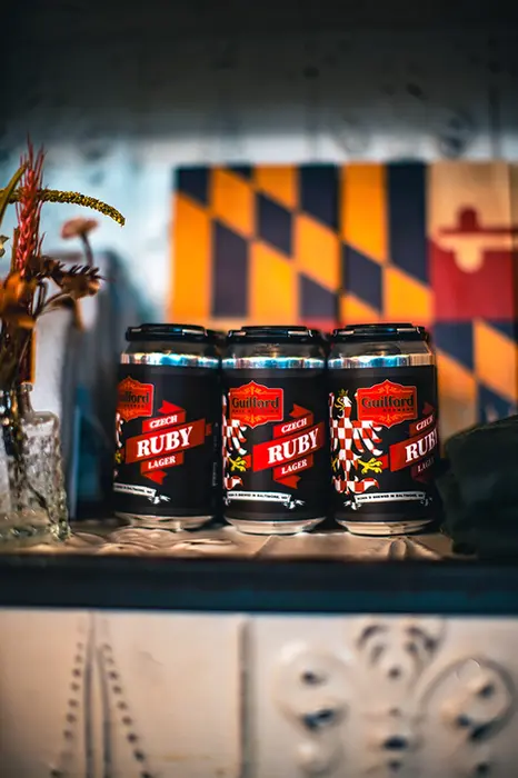 Three "Heavy" beer cans in front of Maryland flag; Guilford Hall Brewery.