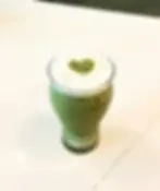 Green matcha latte with heart design on top, sitting on white table