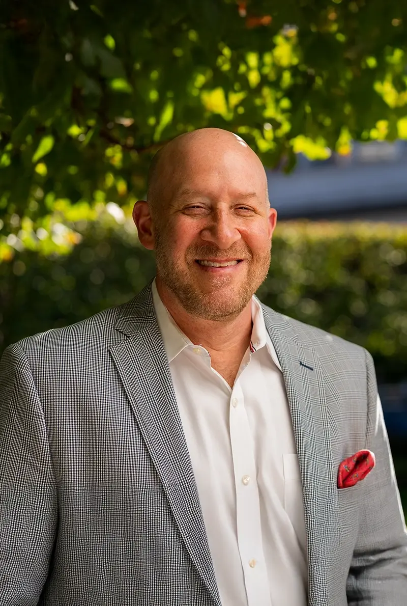 Smiling bald man in a grey suit jacket and red pocket square