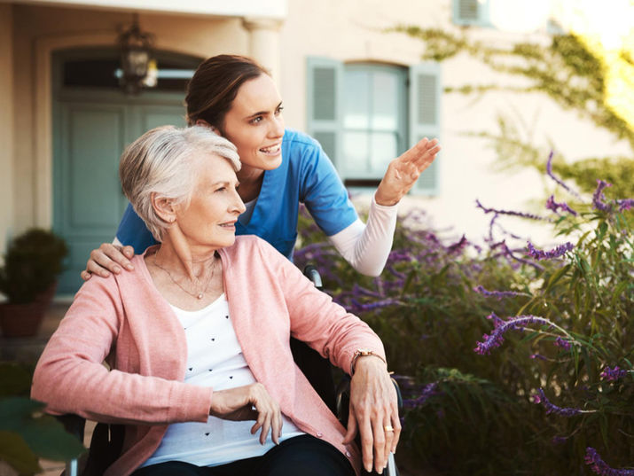 Caregiver points to flowers for elderly woman in wheelchair