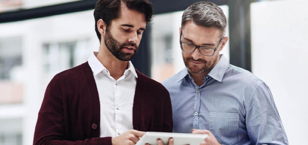Two men in business casual review a tablet in a bright office, focused and collaborative.