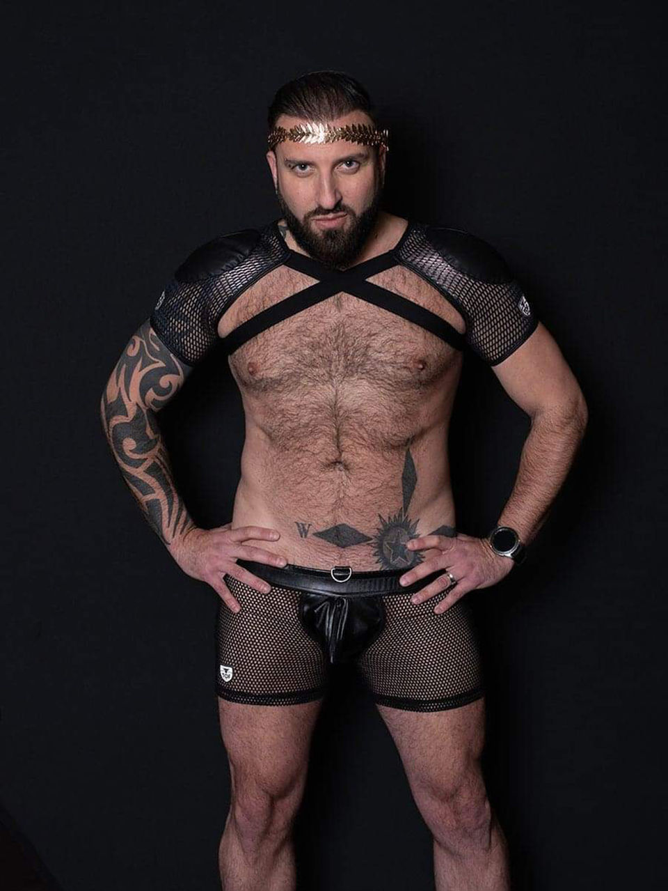 Bearded man wearing black harness, mesh shorts, and head band