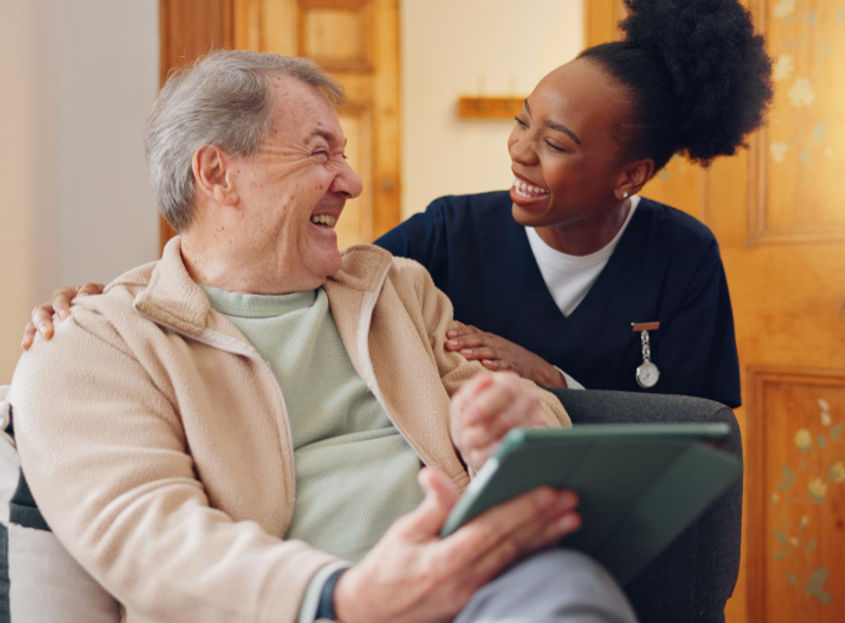 Caregiver and senior man smiling, using a tablet