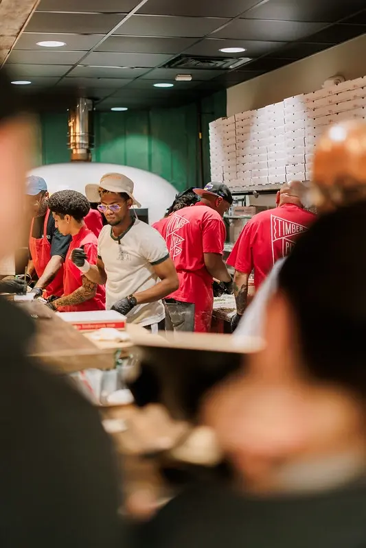 Busy restaurant staff preparing food; employees wearing red shirts and working. Timber Franchise