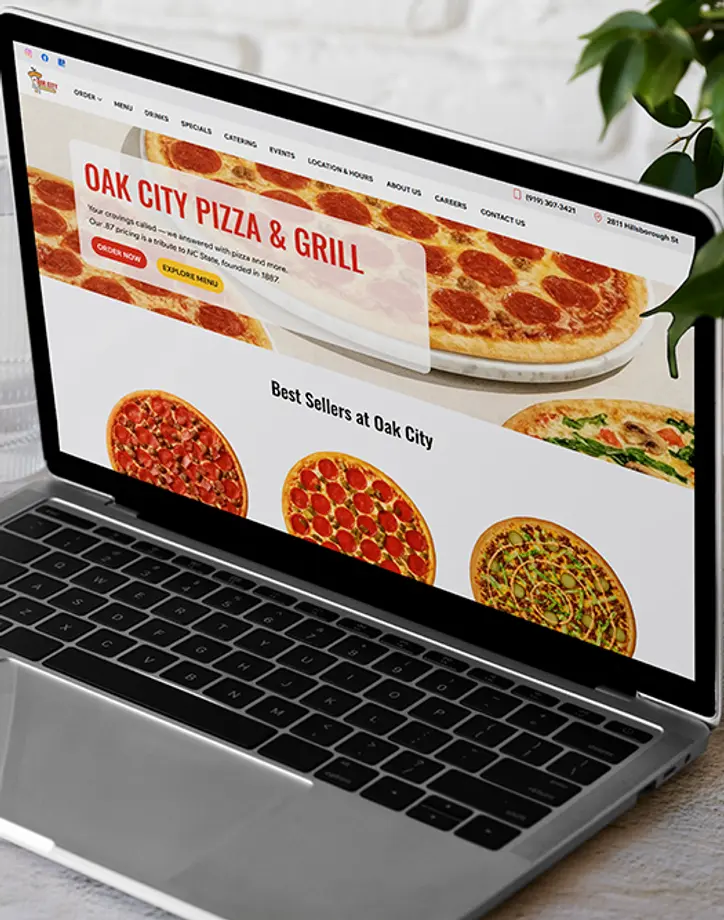 Laptop displaying Oak City Pizza & Grill website with pizza slice nearby