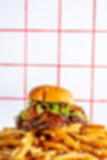 Juicy burger with toppings on golden fries, red grid background.