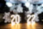 Lit numbers "2022" before a black, white, and silver balloon backdrop with disco balls, under chandeliers, creating a festive atmosphere.