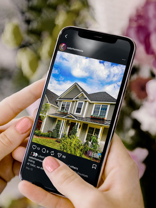A hand holds a phone showing a house under a sunny sky.