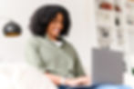 Smiling woman with curly hair working on a laptop at home.