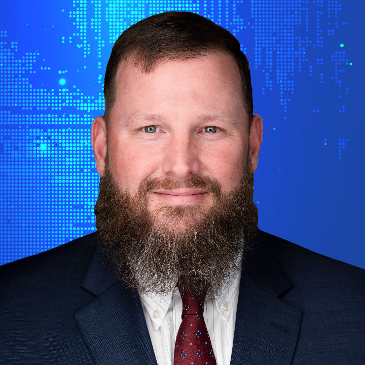 Smiling man with beard, wearing suit and tie, against blue background.