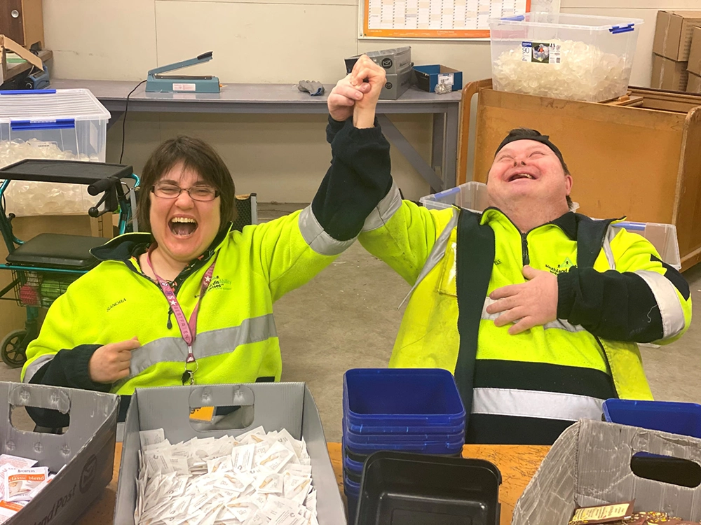 Two happy workers in high-visibility jackets celebrating.