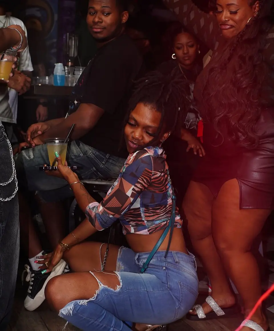 Woman posing with a drink in a crowded club. dev-mugshots