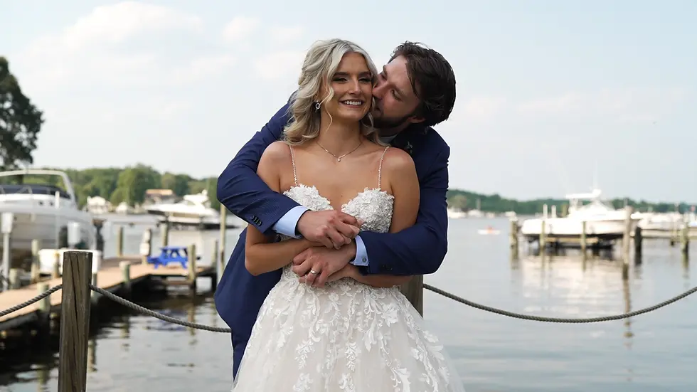 Bride and groom embrace, kiss near water; boats in background, cinematic wedding pricing