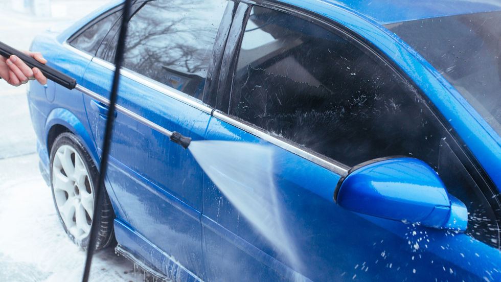 Hand pressure-washes a blue car, spraying suds off the side in a snowy outdoor setting.
