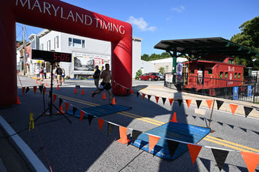 Runners finishing the Mount Airy Mile under a Maryland Timing arch.