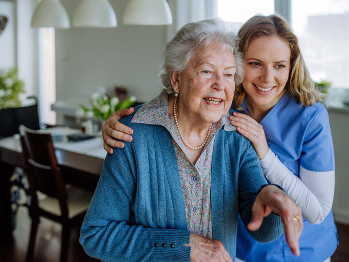 Elderly woman with cane and young caregiver smiling