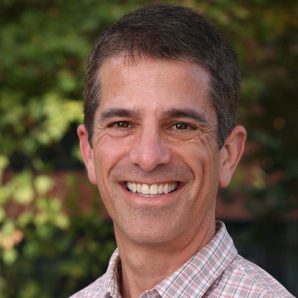 Smiling man with short dark hair in a plaid shirt.