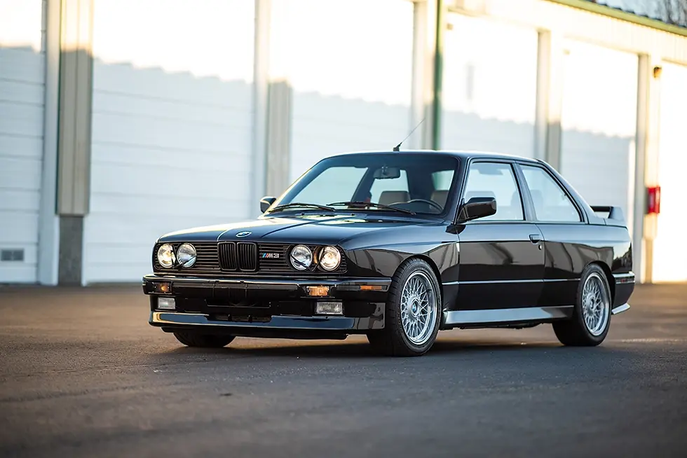Black classic BMW E30 M3 parked in front of white garages