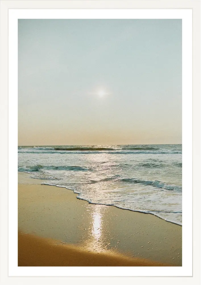 Waves crash the shore under a bright sun; a serene beach scene.