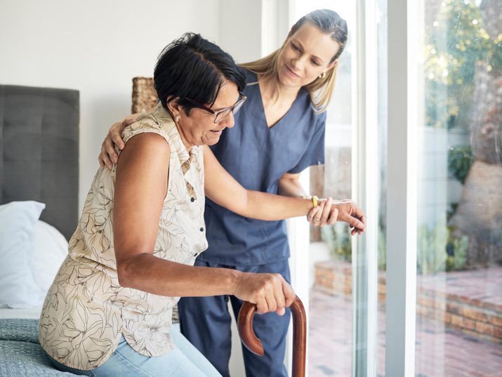 Caregiver assisting elderly woman with cane