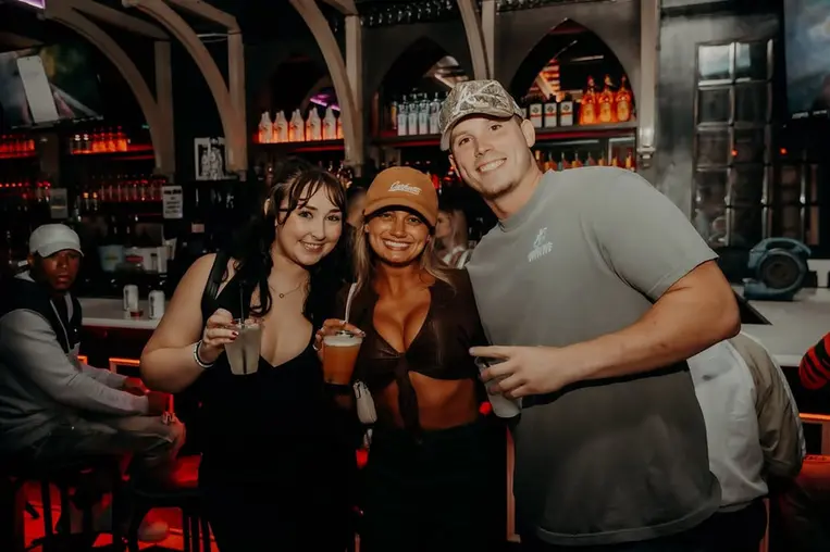 Three friends smiling and posing at a bar with drinks dev-mugshots