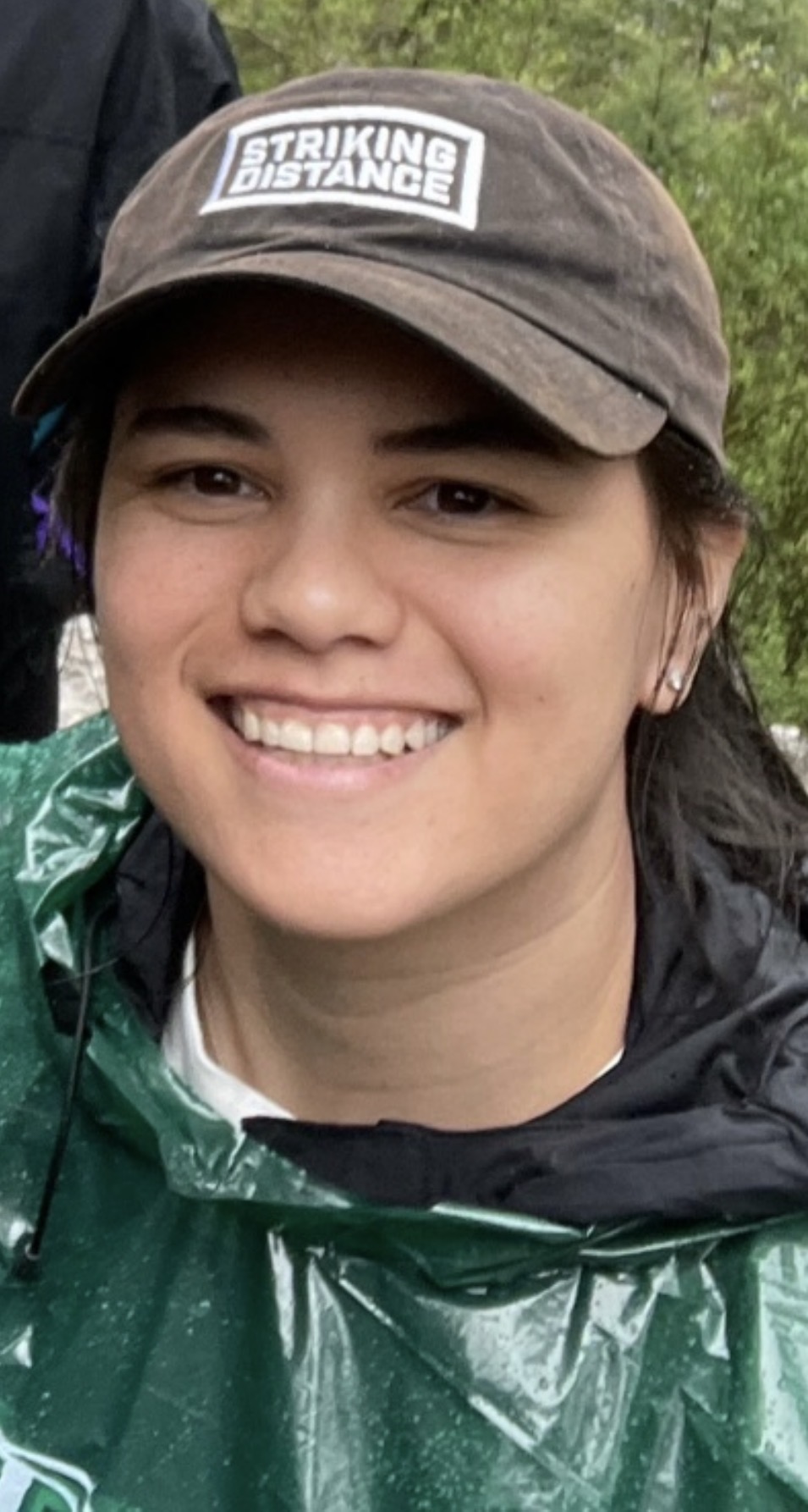 Young woman smiling, "OUTDOORS" on cap, wearing green rain poncho.