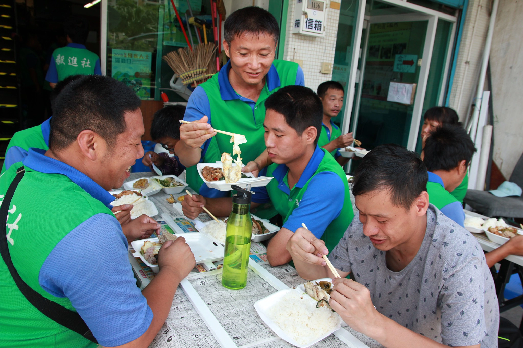 Group of men in green uniforms sharing a meal outdoors.