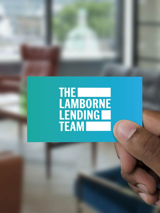Hand holding card: The Lamborne Lending Team, in a blurred office setting.