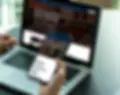 Person using phone and laptop, website interface in the screen, Place Collective website. 