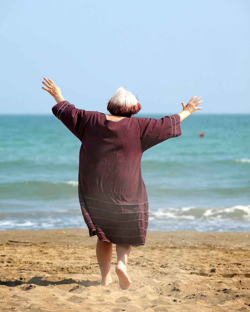The back of a woman (Agnes Varda) dancing in the sand, the sea in front of her