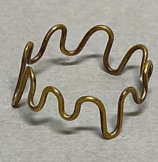 Brass ring with a continuous wave design, photographed from above on a neutral gray surface.