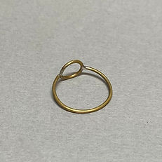 Minimal brass ring with a small central circle accent, placed flat on a neutral gray surface.