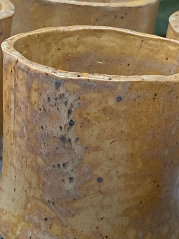Close-up of a handmade yellow-brown ceramic cup showing textured surface and speckled glaze details.