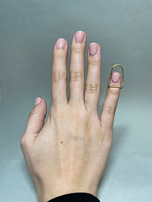 Hand wearing a tall geometric brass ring on the pinky finger against a grey background.