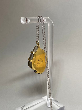 Back view of a pendant necklace featuring a smooth stone held by multiple irregular brass prongs on a silver chain.