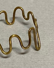 Close-up of a brass wave-shaped ring with visible joint detail, shown on a light gray background.