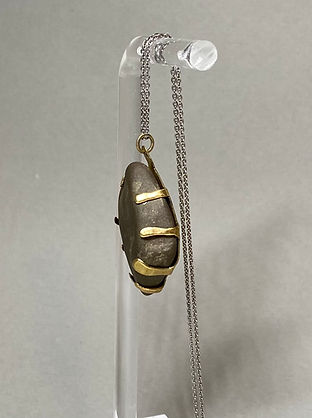 Side view of a pendant necklace with a smooth dark stone secured by sculpted brass prongs on a silver chain.